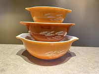 Front view of the three nested Pyrex mixing bowls showing the white wheat graphics on autumn orange and brown backgrounds.
