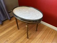 Oblong vintage French accent side table showing white marble top, brass gallery rail, wooden legs, and brass handles on sides.