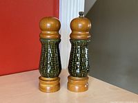 Pair of green ceramic and teak wood salt and pepper shakers side by side showing front and profile view