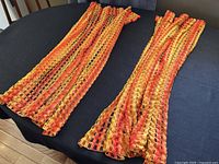 Two orange, red, and yellow net curtains laid out flat on a black surface for size and color display.