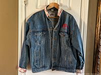 Front view of large XL denim jean jacket with button-up closure, front pockets, and brand embroidery on chest.