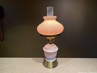 Full view of the hurricane lamp with the light off, showing detailed pattern on poppy white milk glass and brass base.