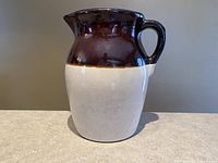 Front view of tan and brown Roseville Pottery stoneware pitcher showing its rustic two-tone color with brown glaze on top and tan lower body.