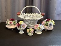 Porcelain braided basket with rose accents and five small porcelain floral bouquet figurines arranged in front of the basket