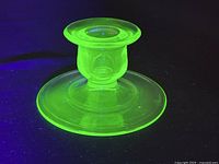 Side and angled view of the green uranium glass candlestick holder glowing under UV light showing shape and glow.