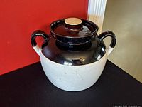 Front side view of vintage double handle bean pot with lid placed on top. The pot is beige with a dark brown glazed top half and handles.