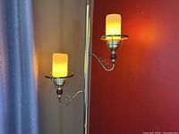 Close-up view of two lit glass lamp shades on a vintage tension pole lamp against a red wall and curtain.