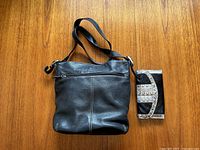 Black leather shoulder purse and matching wallet on wooden surface