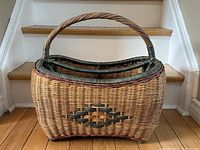 Front angled view of the wicker basket showing the handle, weaving pattern, and feet.