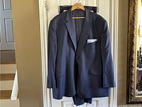 Navy blue suit jacket with white patterned pocket square hanging on a hanger on a door.