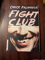 Front cover of Fight Club novel by Chuck Palahniuk showing the book title and smiling man's face.