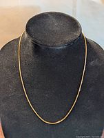 Front view of thin 10K yellow gold box chain necklace displayed on black bust