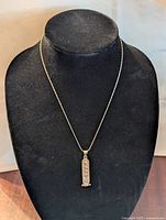 Full view of necklace on display stand, gold-tone chain with pendant hanging down.