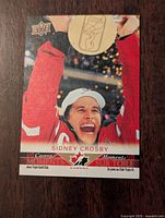 Front of Sidney Crosby 2021-22 UD Canvas Miracle Moments card showing him lifting a trophy wearing Team Canada gear.