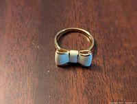 Top view of gold tone ring with white enamel bow on wooden background, showing the bow front detail and ring band.