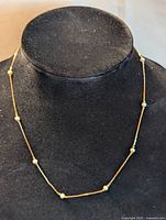 Full length view of a thin gold-tone chain necklace with small white pearls spaced evenly along it displayed on a black velvet neck stand.