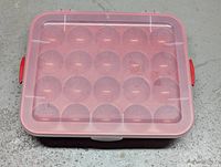 Red plastic ornament storage container with translucent pink lid, shown closed.