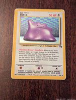 Front of damaged Ditto holo Pokemon card showing purple Ditto with 50 HP and holographic background with checkered pastel colors.