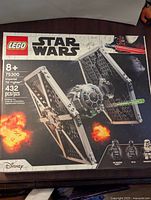 Front of the LEGO box showing Star Wars Imperial TIE Fighter model with fire and space background, LEGO and Star Wars logos, Disney branding.