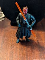 Front view of Darth Maul figure holding double-bladed red lightsaber in both hands, showing black robes and detailed face paint.