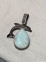 Top and front view of sterling silver dolphin pendant with a polished teardrop larimar stone set below the dolphin figure.