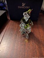 Front view of Peter Pan figurine seated on rock base with original Swarovski box behind.