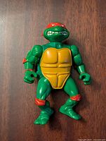 Front view of the green Teenage Mutant Ninja Turtles Raphael figure with red bandana, yellow chest plate, and red pads on elbows and knees.