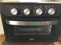 Front view of the black Master Chef toaster oven showing four silver control dials for temperature, timer, function selection, and oven heat settings.