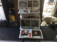 Nine Funk and Wagnalls Family Library of Great Music albums, volumes 14 through 22, arranged on a chair and table, covers showing portraits of composers such as Mozart, Beethoven, Haydn, and Dvořák.