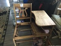 Photo of antique wooden left hand school desk with missing seat, showing lyre-shaped backrest and storage shelf beneath desk surface.