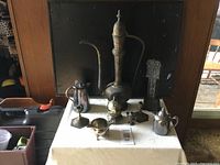 Photo of the full group of antique metal items on a cloth-covered table in front of a dark background