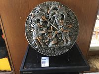 Front view of the heavy Aztec-style circular sculpture on black wooden stand showing detailed carvings of figures and geometric patterns.