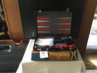 Backgammon game set in open black carrying case showing the playing board, checkers, and dice cups inside the case.