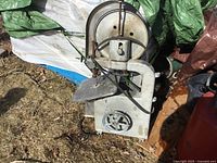Metal band saw showing cutting table, wheel housing and frame, placed outdoors on grass, condition used with signs of wear and weather exposure.