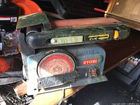 Three different angled photos of a Ryobi heavy duty belt sander grinder showing 4 x 36 inch sanding belt, front grinder wheel, and power switch. Tool appears used with some surface wear.