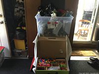 Full shot of clear plastic bin filled with artificial flowers in black, white, and red, stacked on a large cardboard box.