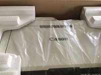 Canon printer packaged in foam and plastic wrapping inside the box, showing the Canon logo on the device.