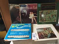 Photo showing 5 vinyl classical music albums with worn covers, titles include Godard 'King of the Oboe,' Swan Lake by Tchaikovsky, Johann Sebastian Bach collection, Waltzing with the Wurlitzer, and another classical piece with a painting on the cover.