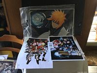 Three anime prints including Ichigo Kurosaki from Bleach, Attack on Titan characters, and a third group print on a wooden chair and table.