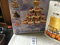 Box of Wilton Cupcakes N More Dessert Stand for cupcakes and partial view of Maxwell & Williams glass juice jar and metal stand with tap.