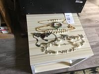 Photo of vintage jewelry laid out on a light-wood side table containing necklaces and a bracelet.