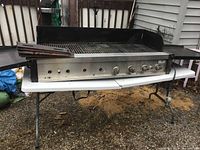 Full view of grill on folding table, showing cooking area, front control panel and side shelves