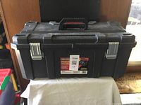 Closed view of large black Benchmark heavy duty plastic toolbox showing metal latches and handle on a white cloth-covered surface.