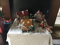 Photo of three light-up ceramic Christmas village houses and horse-drawn carriage figurine with electrical cords on a white surface.