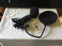 Audio-Technica microphone laid flat on white cloth with foam windscreen and circular pop filter alongside.