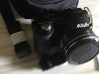 Front and top angle view of black Nikon Coolpix digital camera showing lens, logo, and hand strap.