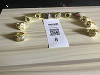 11 collector rings arranged in a semi-circle on a wooden surface, showing various emblems and colors including gold, silver, blue, red, and black accents.