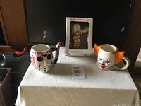 Wide shot of all three items on white cloth: Two horror-themed mugs and boxed Sparky bobblehead.