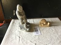 Photo showing the two soapstone carvings placed on a white cloth, the larger figure and the smaller igloo scene.