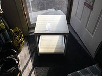 Front view of solid metal frame stand with light wood shelves under natural light, showing the square shape and two shelf levels.